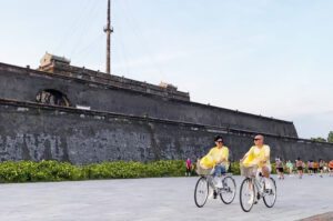 a couple of people riding bicycles in front of a stone wall