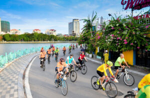 The leisurely atmosphere of cycling in Hanoi, particularly focusing on the flower-carrying bicycles along Thuy Khue – Mai Xuan Thuong streets. These bicycles contribute to a unique characteristic of the city with their vibrant colors and serene presence, alleviating the fatigue of street vendors and fostering a sense of harmony and freshness in the neighborhood.